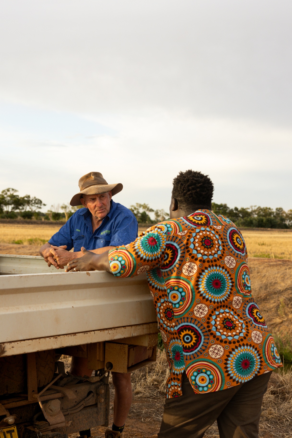 Two farmers talking beside a farm ute in a harvested field.